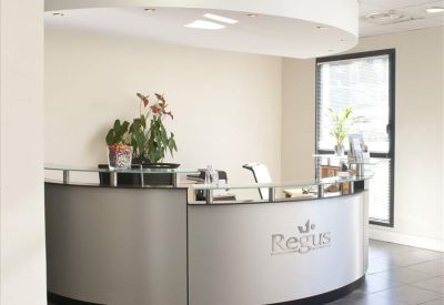 Professional reception desk with a curved silver facade and green indoor plants.