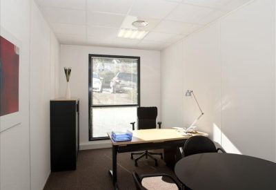 Bright workspace featuring a desk, a round meeting table, and a window overlooking greenery.