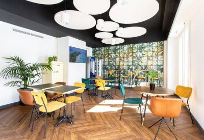 Bright communal lounge with colorful chairs, wooden flooring, and decorative ceiling light fixtures.