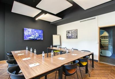 Professional meeting room with a U-shaped wooden table, wall-mounted screen, and herringbone wood floor.
