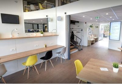 Coworking area with long wooden desks and yellow and black chairs.