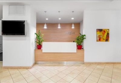 Bright reception area with a minimalist white desk, wood paneling, and indoor plants.