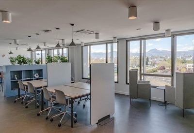 Bright communal coworking space with individual desks, privacy screens, and mountain views.