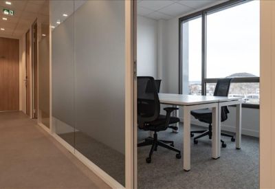 Private glass-walled office suite with a white desk and ergonomic black chair.