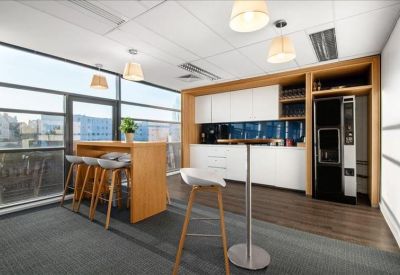 Communal break area with a wooden high table, white cabinetry, and large windows.