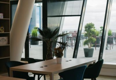 Bright coworking area with a wooden table and a view of a rooftop terrace through large windows.
