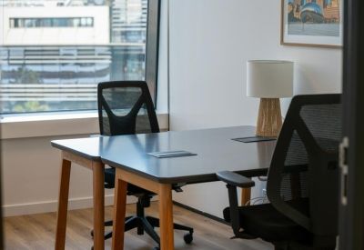 Private office workspace with a dark desk, mesh chair, and views of the city through the window.
