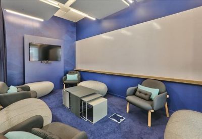 Relaxation lounge with blue walls, comfortable grey armchairs, a white board, and a television screen.