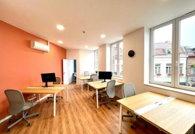 Sunlit coworking space with multiple workstations and large windows overlooking the street.