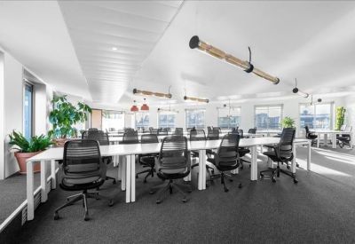 Open-plan office with rows of white desks, black mesh chairs, and overhead tubular lighting.