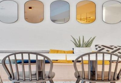 Close-up of a dining area with wooden spindle chairs and a row of five mirrors on the wall.