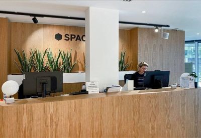 Modern wooden reception desk with snake plants and the building logo in the background.