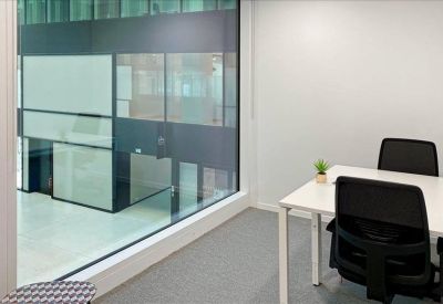 Private glass-walled office with two desks and view of an interior atrium.
