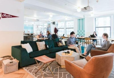 Bright coworking area with a dark green velvet sofa, leather armchairs, and a geometric rug.