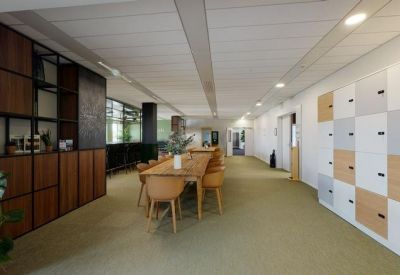 Sleek office corridor featuring a long wooden meeting table, accent shelving, and integrated lockers.