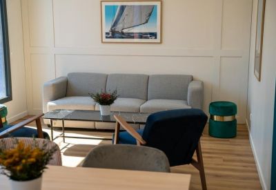 Lounge area with a gray sofa, navy armchairs, and nautical wall art.