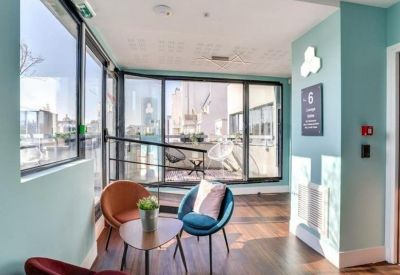 Sunlit breakroom corner with blue and orange chairs overlooking a balcony.