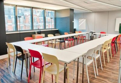 Classroom-style meeting room with a U-shaped white table and multi-coloured chairs.