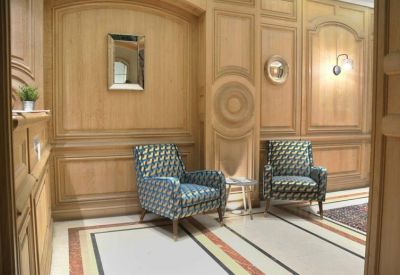 Lounge area with ornate wood paneling and two blue patterned armchairs.