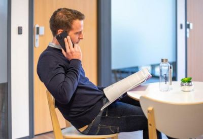 Relaxed breakout area with a person on a call near a wooden table and glass partitions.