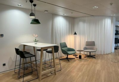 Breakout area with high wooden table, stools, and plush armchairs near white curtains.