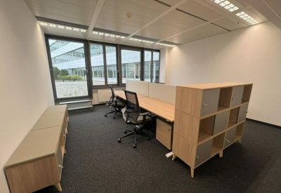 Bright private office with wooden desks and shelving units next to large windows.