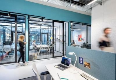 Open-plan office area with white desks, glass partitions, and turquoise accents.