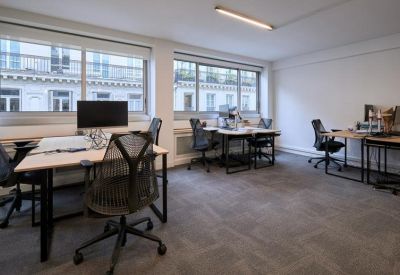 Bright open-plan office with ergonomic chairs, light wood desks, and large windows.