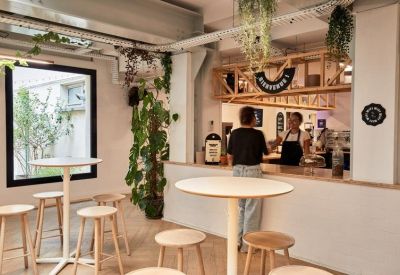 Modern café area with high tables, wooden stools, and a service counter.