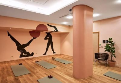 Yoga and wellness studio with peach walls, artistic wall murals, and exercise mats on a wooden floor.