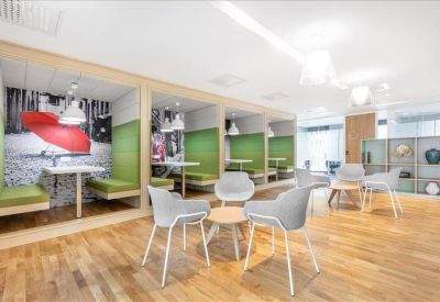 Bright coworking area featuring green semi-enclosed booths and modern grey armchairs.
