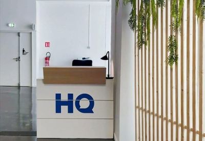 Reception desk with bold blue HQ branding and a decorative wooden slat wall with hanging plants.