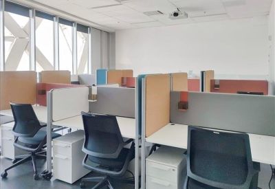 Open-plan office with white desks and black ergonomic chairs near large windows.