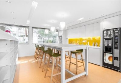 Bright kitchen and breakout area with a high communal table, wooden stools, and a yellow tiled backsplash.