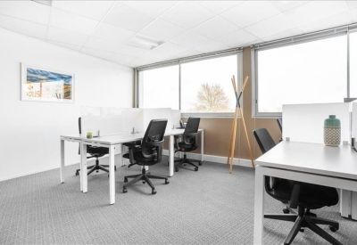 Bright open-plan workspace with white desks, ergonomic black chairs, and large windows.