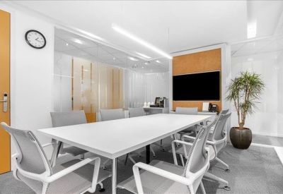 Modern meeting room with a large white table, grey chairs, a wall-mounted screen, and a potted plant.