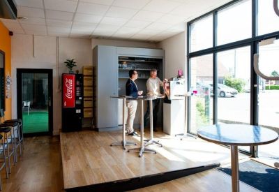 Bright communal kitchen and breakout area with high tables, wooden flooring, and a glass storefront.