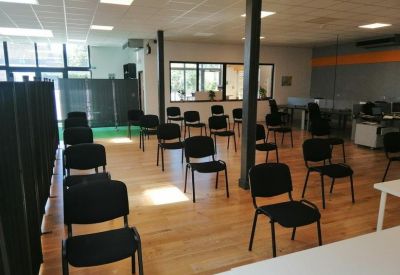 Large training room with rows of black chairs on wooden flooring and bright ceiling lights.