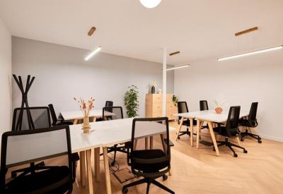 Bright open-plan office with white desks, black ergonomic chairs, and wooden flooring.