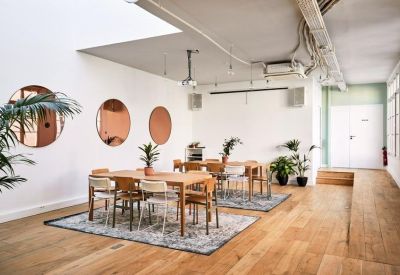 Spacious coworking lounge with circular mirrors, wooden tables, and indoor plants.