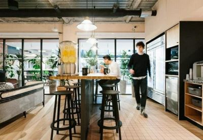 Communal kitchen and break area with high stools, wooden floors, and a juice dispenser.