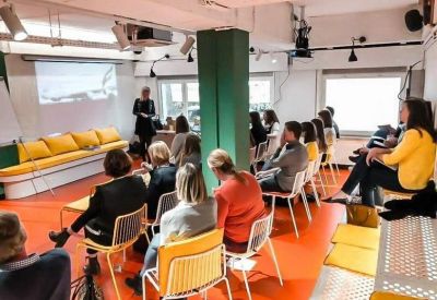 People attending a presentation in a vibrant communal space with orange floors and a green pillar.