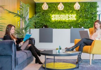 Reception area with green wall and Sundesk logo, two women working on laptops.