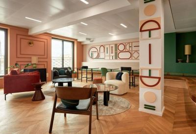 Sunlit lounge area featuring eclectic furniture, a patterned pillar, and warm wood floors.