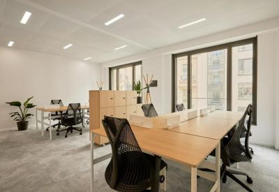 Open-plan office with light wood desks, ergonomic black chairs, and large windows.
