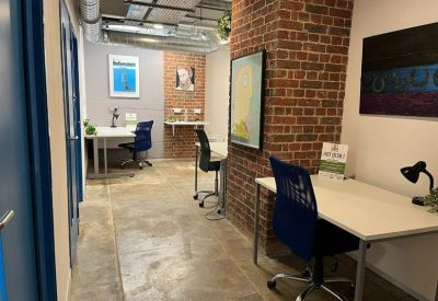 Office workspace with individual desks and ergonomic chairs set against an exposed brick wall.