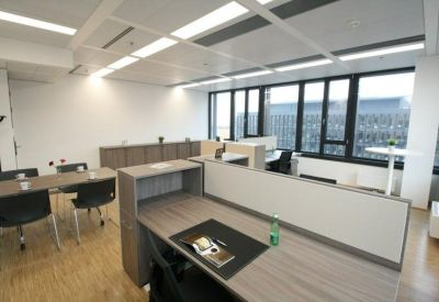 Open-plan office with grey partitions, wooden desks, and large windows.