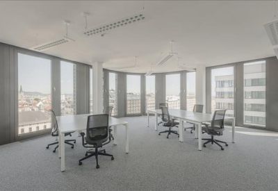 Spacious open-plan office with white desks and large windows.