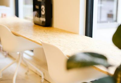 Close-up of a window-side workstation with white chairs and a light wood-textured desk.