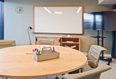 Meeting room with round wooden table, whiteboard, and television screen.